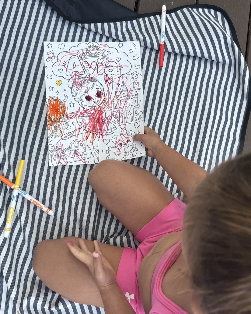 A young girl coloring her personalized coloring page outside on a striped blanket