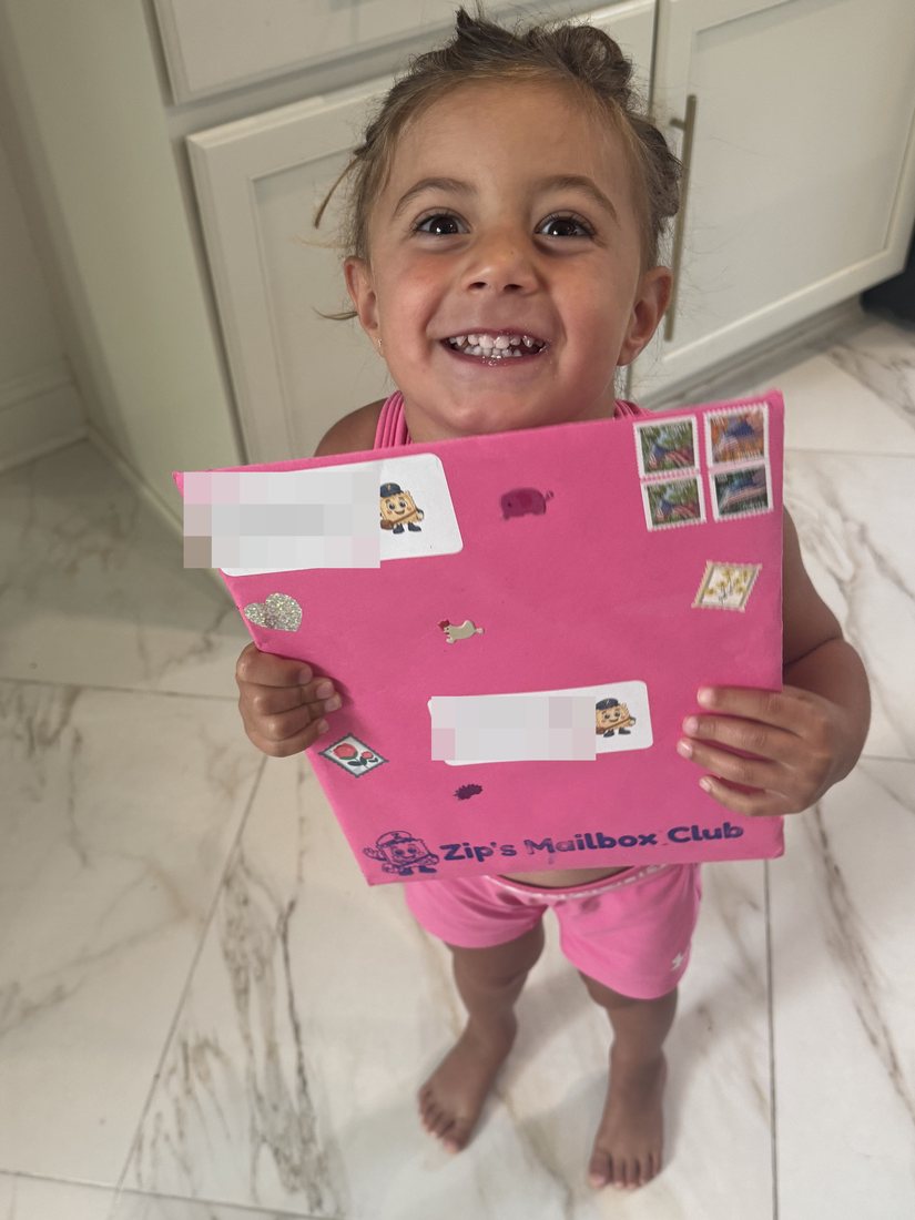 A little girl beaming as she holds her big pink envelope from Zip