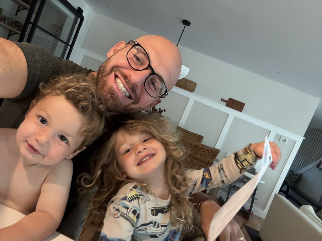 A dad and his two young children smiling together, one holding a Zip letter