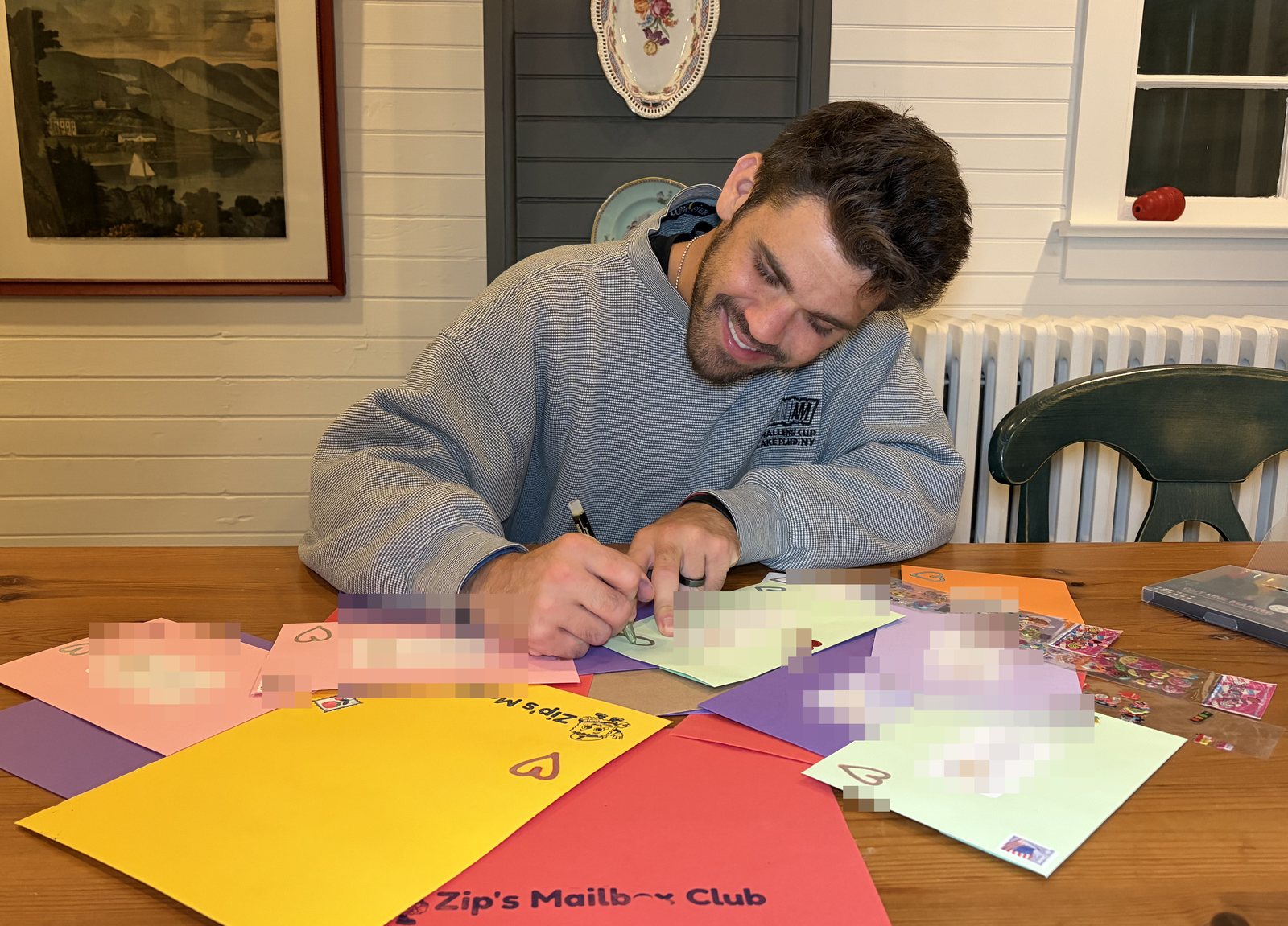 The founder of Zip's Mailbox Club smiling while hand-addressing a table full of bright envelopes