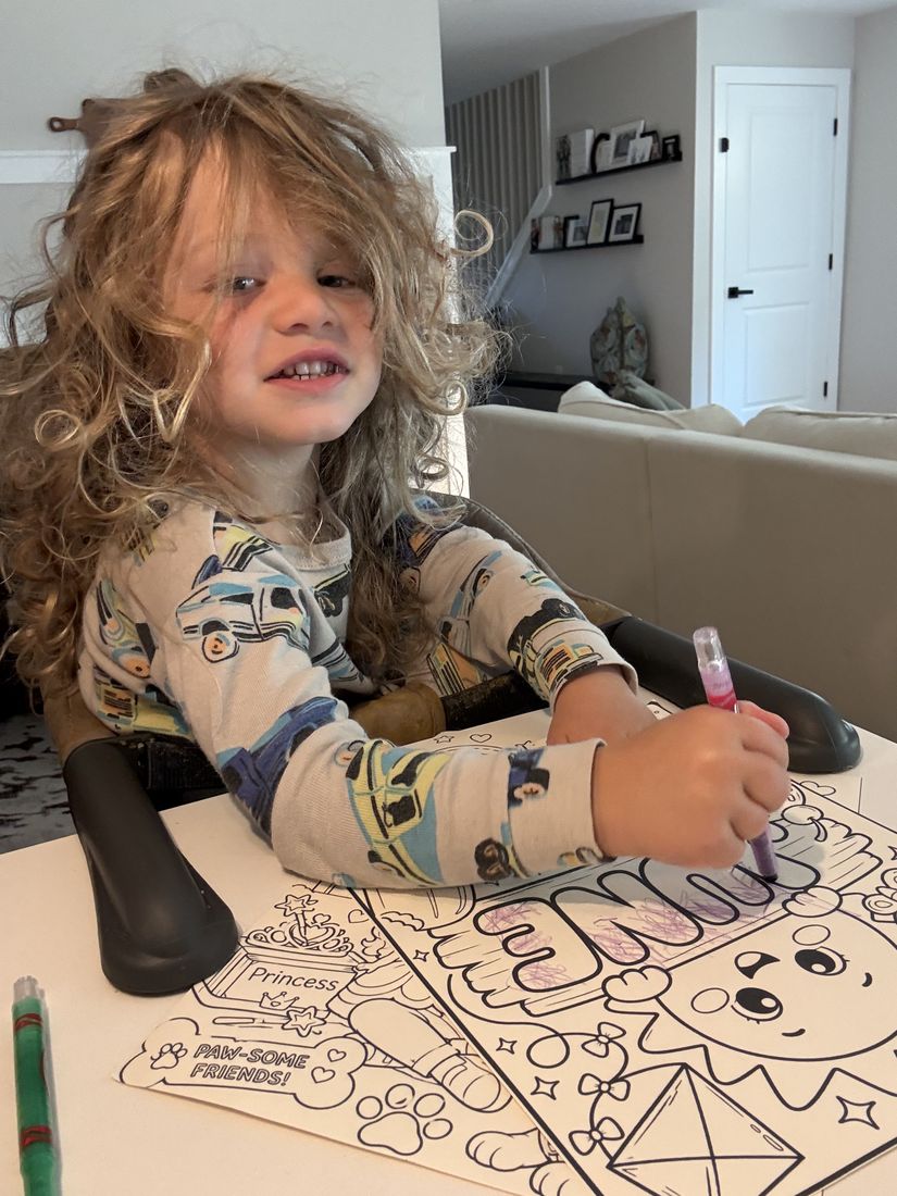 A child smiling while coloring an activity page with a marker