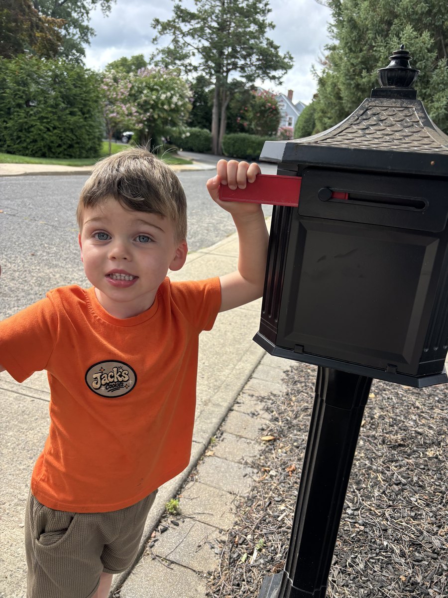 A young boy grinning as he raises the red flag on a black mailbox