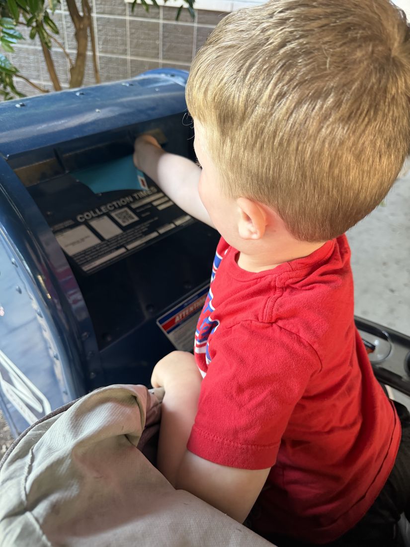 A young boy posting an envelope into a blue USPS collection box