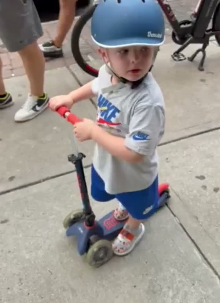 A young boy in a helmet on his scooter, out hunting for a mailbox