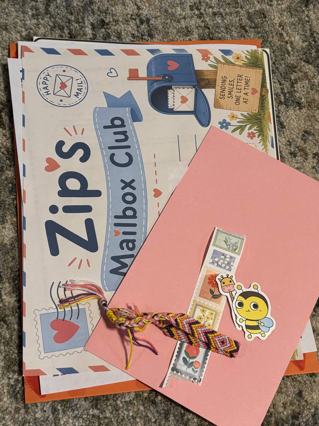 An opened Zip's Mailbox Club delivery: the illustrated letter, a bright envelope, a strip of decorative stamps, stickers, and a woven friendship bracelet