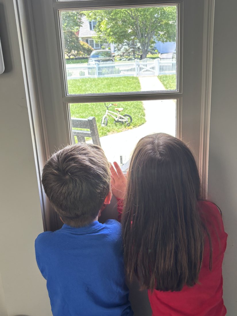 A boy and his cousin at the front window, watching the street for the mail to arrive